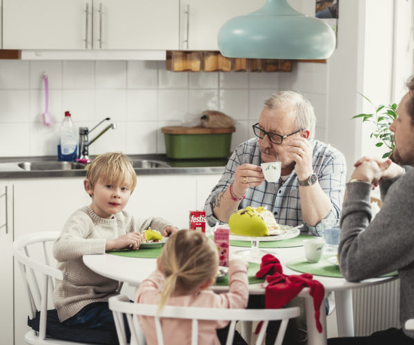Hyresgäst sitter med barn och barnbarn vid köksbordet och fikar